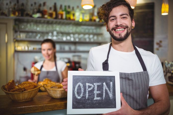 Smiling waiter showing slate with open sign in café